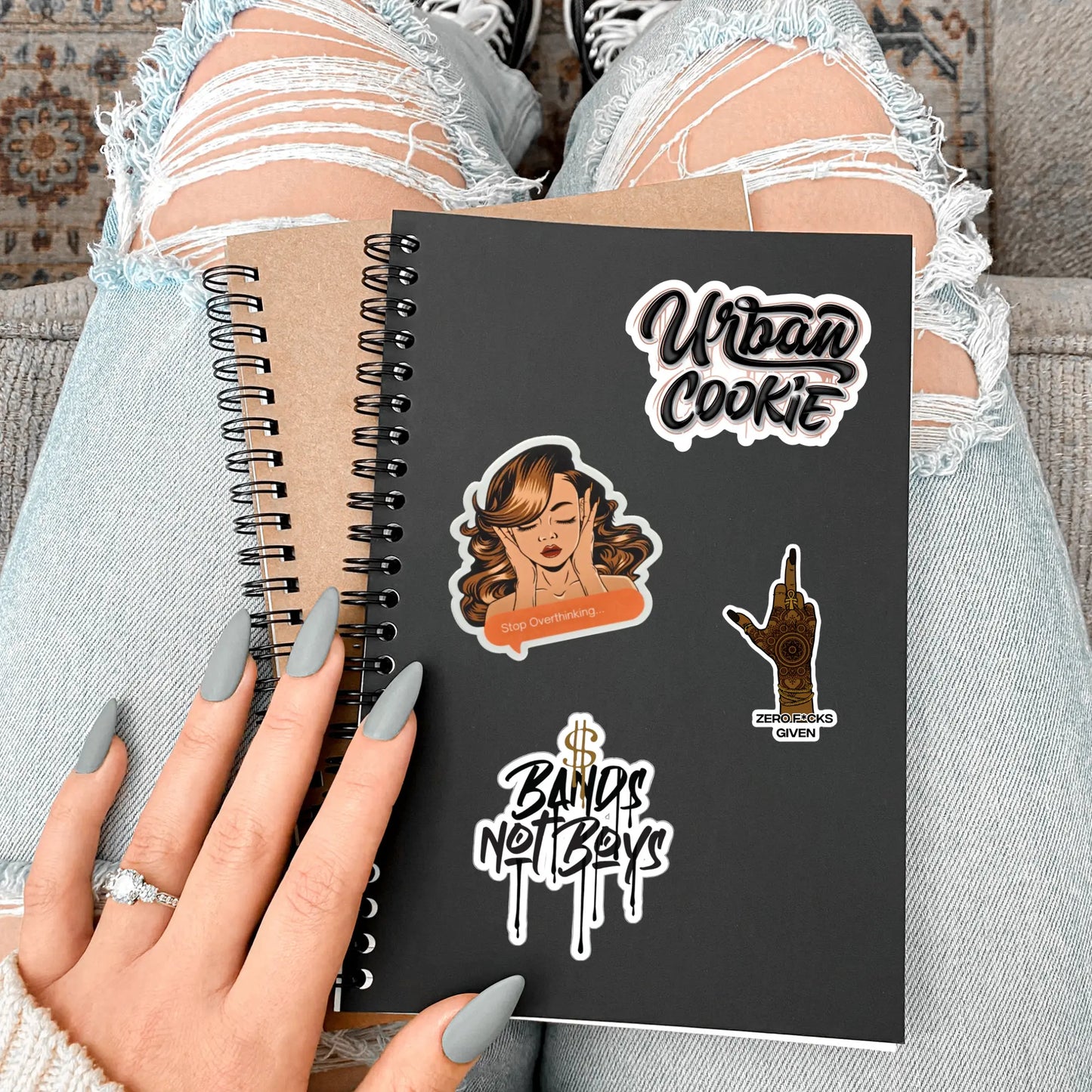 Urban Cookie Overthinker, Zero F*cks, Bands Not Boys and, Urban Cookie vinyl stickers on a spiral bound journal on the lap of a female with manicured nails.