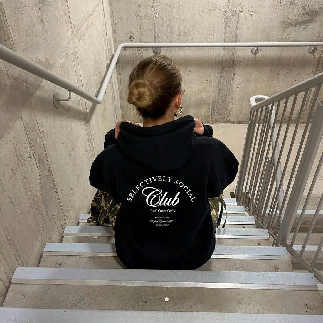 Person sitting in a staircase wearing Urban Cookie's Selectively Social Club Hoodie