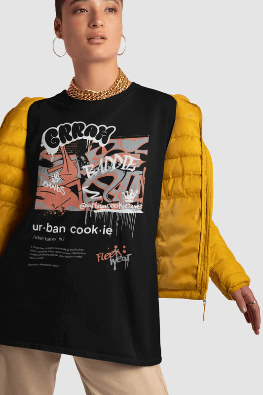 Edgy girl posing with a buzz cut and gold jewelry wearing a oversized Black Urban Cookie Graffiti T-shirt with a yellow jacket and tan pants