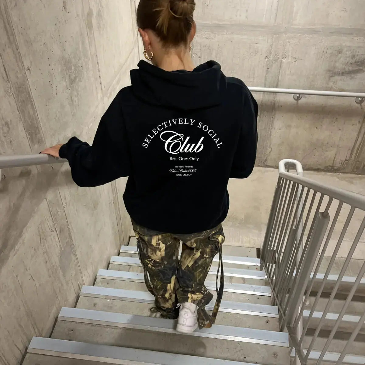 Person wearing a black hoodie with 'SELECTIVELY SOCIAL Club' text, climbing stairs.