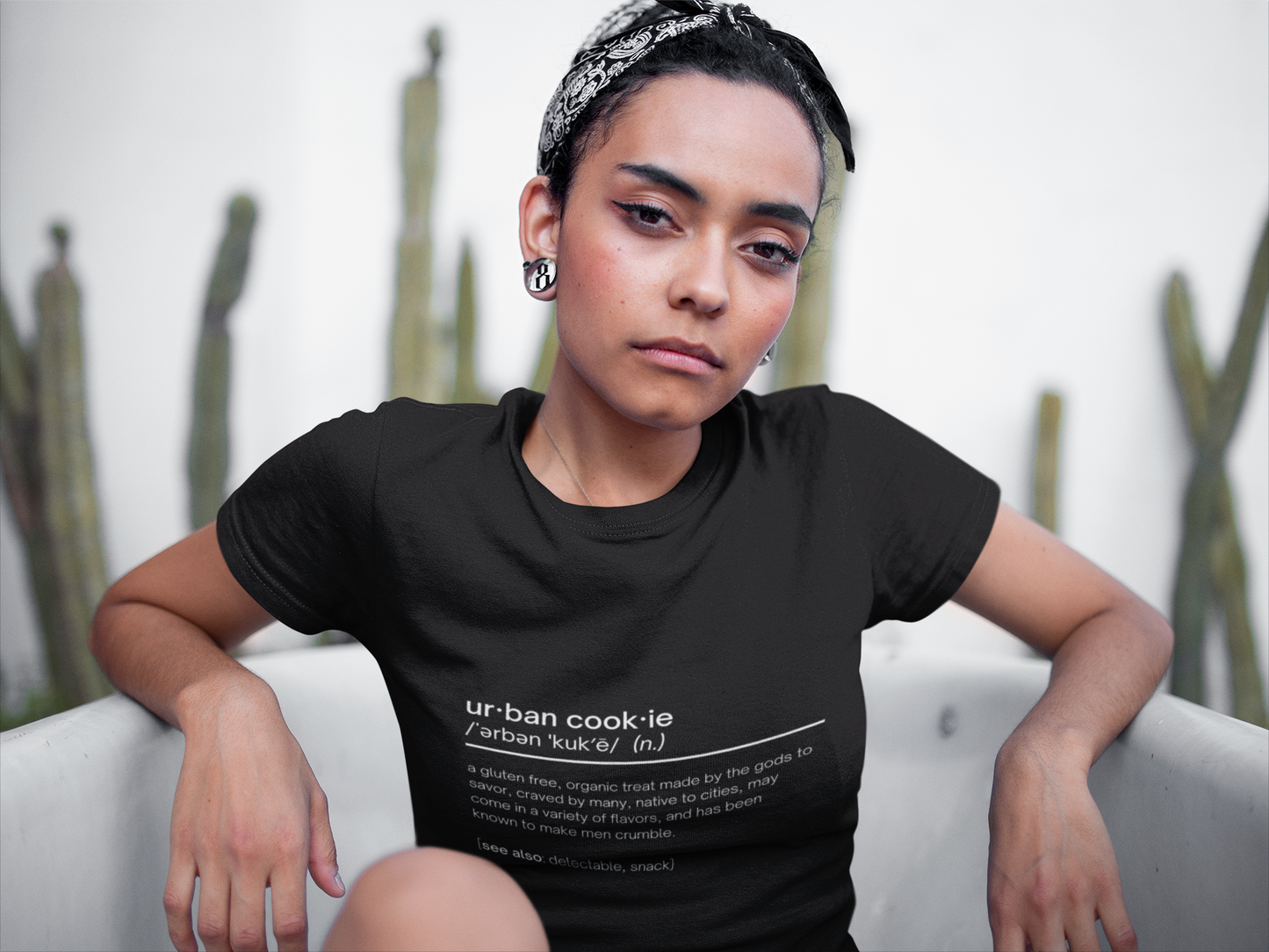 A girl with a serious face, wearing an Urban Cookie definition tee sitting in a bathtub wearing a black and white bandana. Blurry wallpaper in the background.