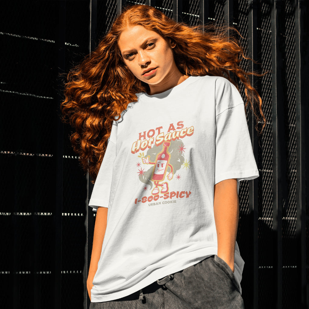 Edgy girl with a serious face, hands in her pockets, Septum piercing and Red hair standing beside a fence wearing an Urban Cookie Spice It Up Tee featuring a vintage cartoon character with "Hot As Hot Sauce, 1-800-SPICY and Urban Cookie text.